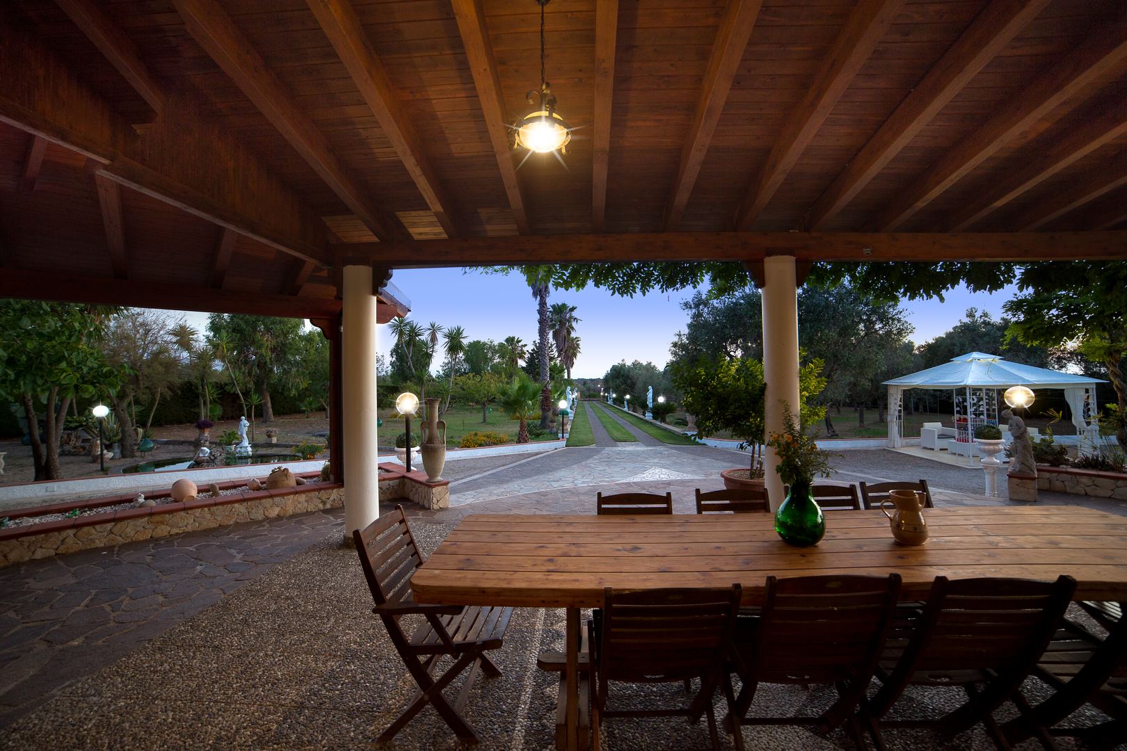 Portico di sera — tavolo illuminato e viale sullo sfondo